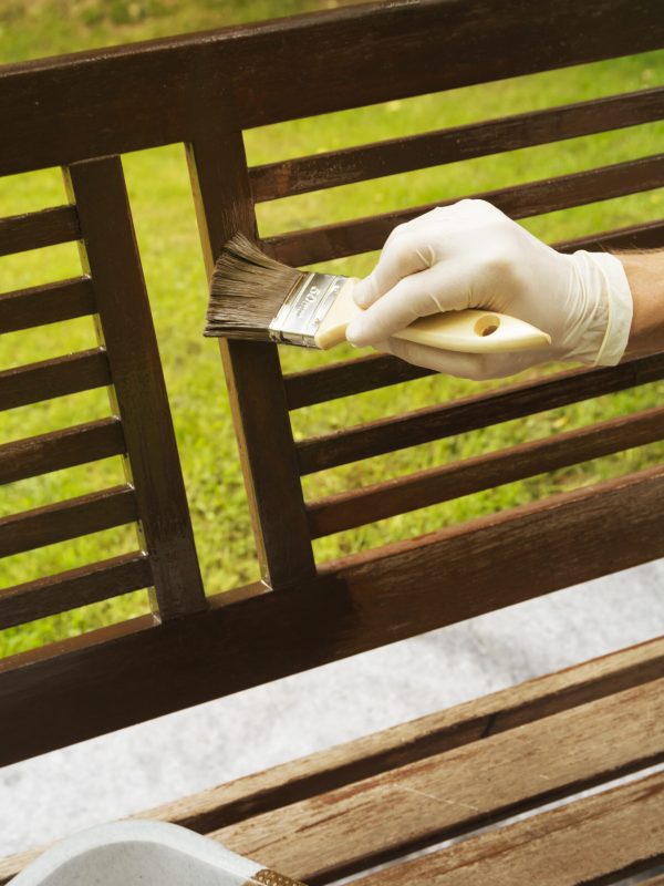Man applying glaze on wooden bench, partial view