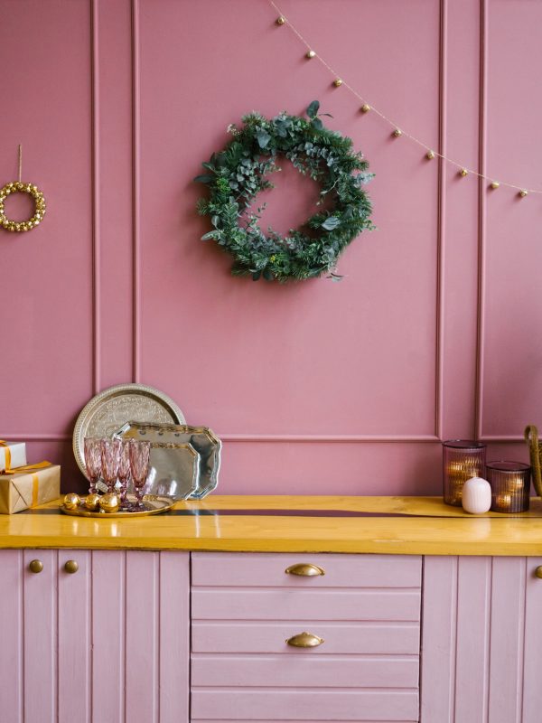 The concept of the winter holidays. Festive Christmas decorations in the pink kitchen with a handmade wreath of fir branches. Christmas / new year composition.